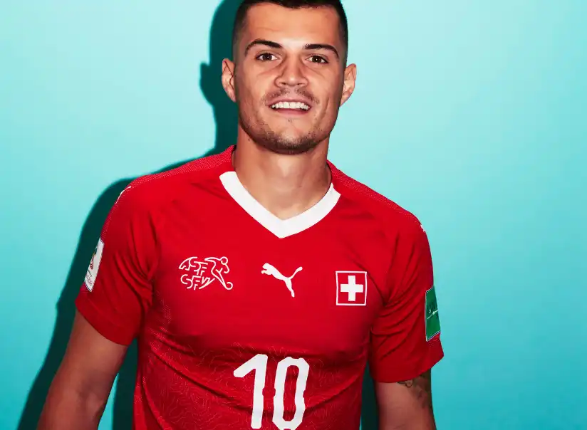 瑞士國家隊球員格蘭尼特·扎卡(Granit Xhaka)身穿瑞士紅色國家隊球衣拍攝官方形象照,背景為藍綠色攝影棚背景。